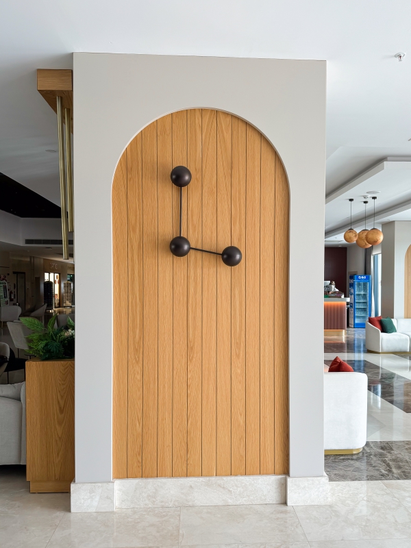 Close Up Of A Modern Architectural Feature With A Wooden Arched Panel And A Minimalist Black Light Fixture.